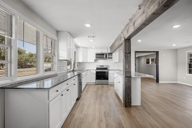 kitchen featuring white cabinetry, stainless steel appliances, backsplash, dark stone countertops, and light hardwood / wood-style floors