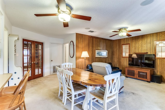 dining room featuring light carpet, wooden walls, french doors, and a textured ceiling