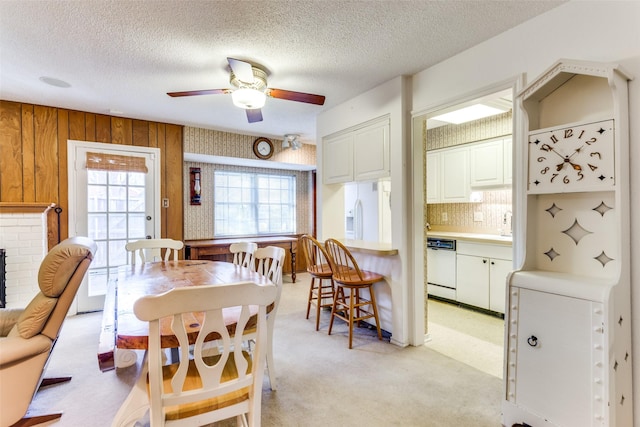 dining room with a textured ceiling, light colored carpet, ceiling fan, and wood walls