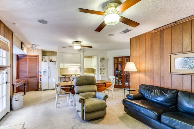 carpeted living room with ceiling fan, a textured ceiling, and wooden walls