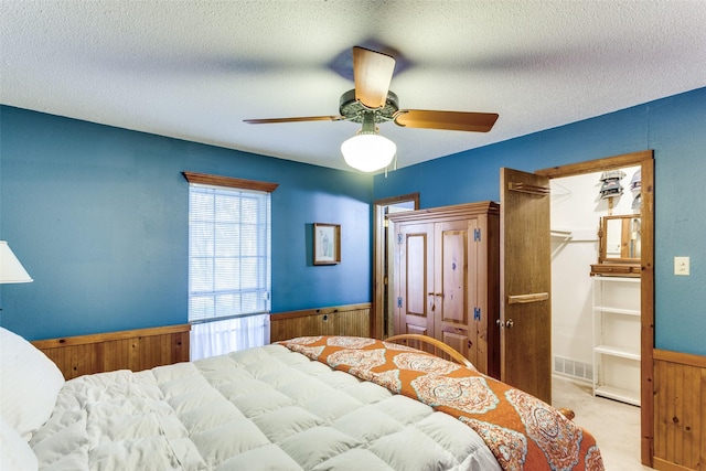 carpeted bedroom with wooden walls, ceiling fan, and a textured ceiling