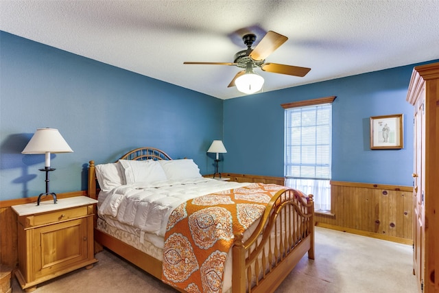 bedroom with a textured ceiling, light colored carpet, ceiling fan, and wooden walls