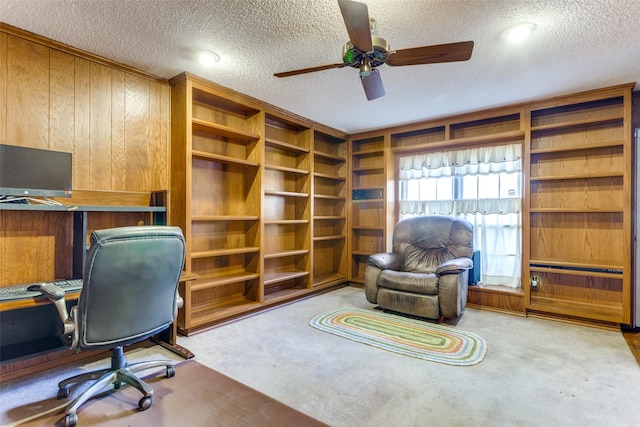 office area with a textured ceiling, light colored carpet, ceiling fan, and wooden walls