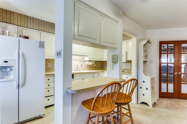 kitchen featuring sink, backsplash, a kitchen bar, white appliances, and french doors