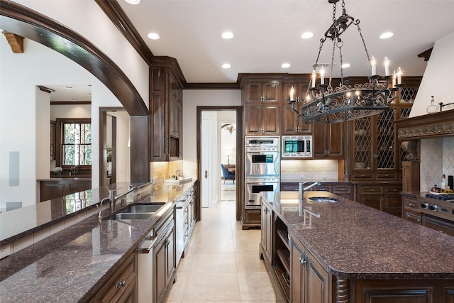 kitchen featuring tasteful backsplash, hanging light fixtures, sink, stainless steel appliances, and a center island with sink