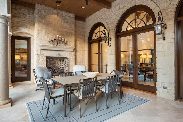 tiled dining room with wood ceiling, decorative columns, an outdoor stone fireplace, french doors, and beam ceiling