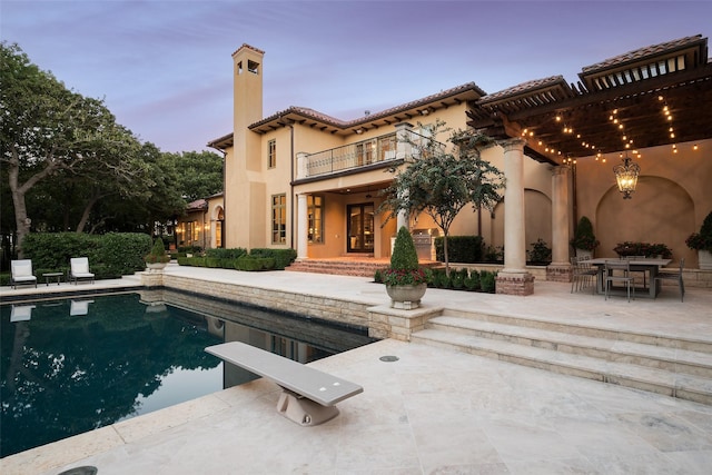 back house at dusk featuring a balcony, a patio area, and a pergola