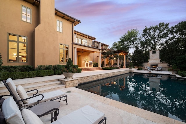 pool at dusk featuring an outdoor fireplace and a patio area