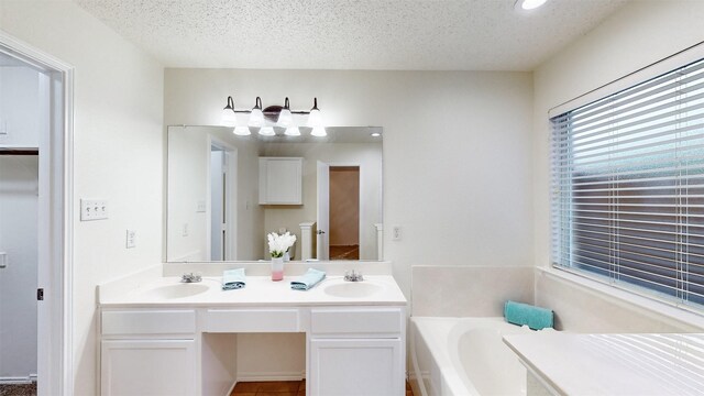 bathroom featuring vanity, a bath, and a textured ceiling