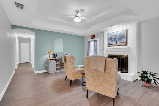 living area featuring ceiling fan, light hardwood / wood-style floors, a raised ceiling, and a fireplace