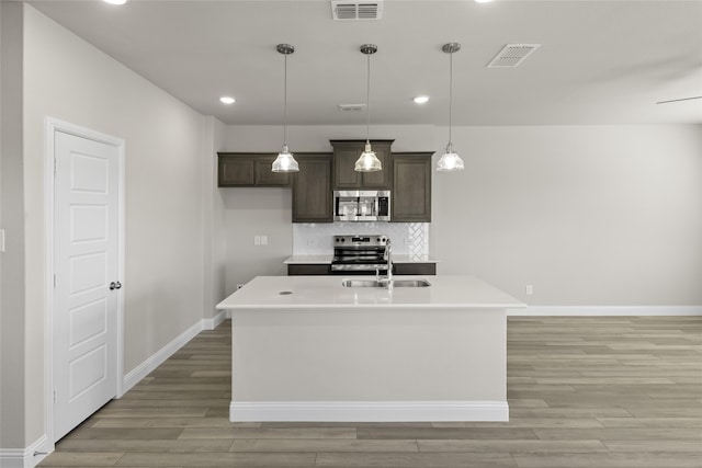 kitchen with appliances with stainless steel finishes, hanging light fixtures, dark brown cabinets, and a kitchen island with sink