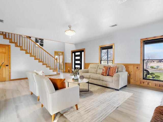 living room featuring a wainscoted wall, light wood-style flooring, visible vents, and stairway