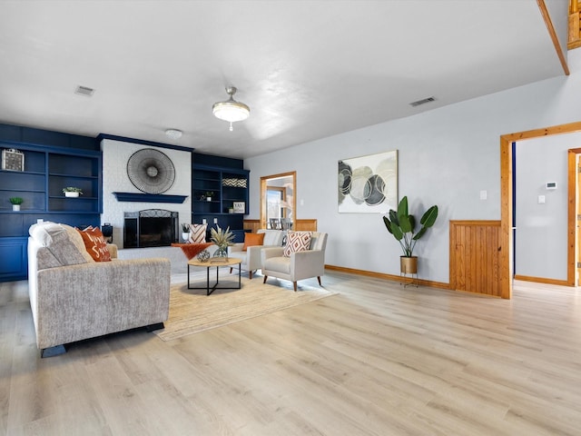 living room with light wood-type flooring, a fireplace, visible vents, and built in features