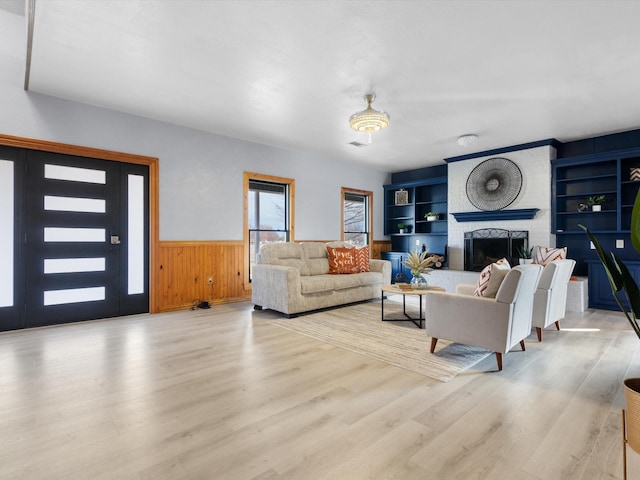 living area featuring wood walls, wood finished floors, built in features, wainscoting, and a brick fireplace