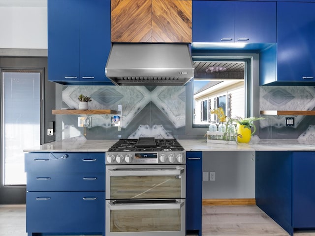 kitchen featuring range with two ovens, a wealth of natural light, wall chimney range hood, and blue cabinetry