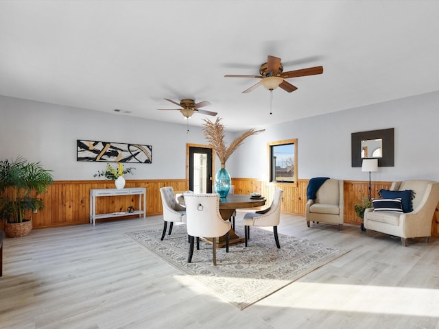 dining space with light wood-type flooring, visible vents, and wainscoting