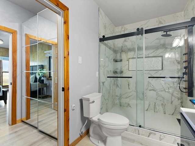 full bath featuring toilet, a marble finish shower, baseboards, and wood finished floors