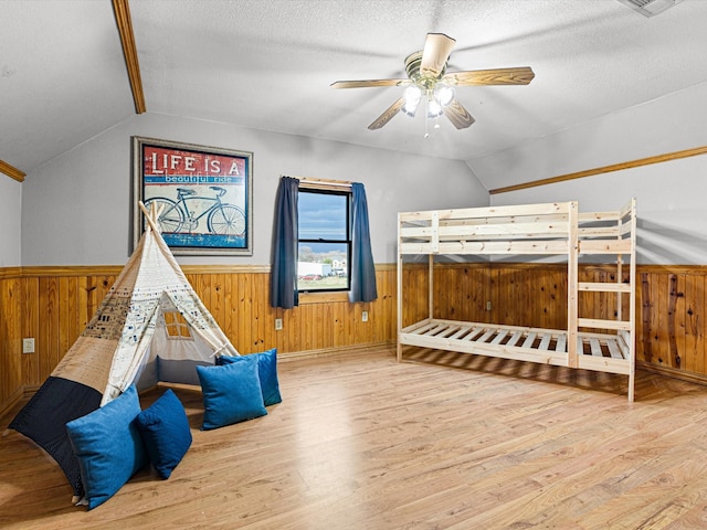 bedroom featuring a textured ceiling, wooden walls, a wainscoted wall, wood finished floors, and vaulted ceiling