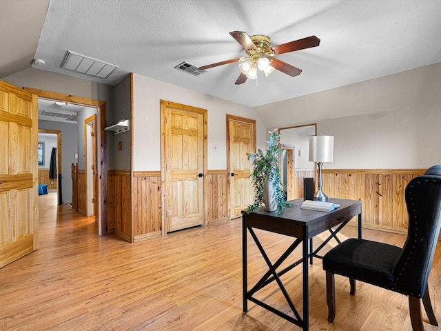 office with lofted ceiling, a wainscoted wall, visible vents, and light wood-style flooring