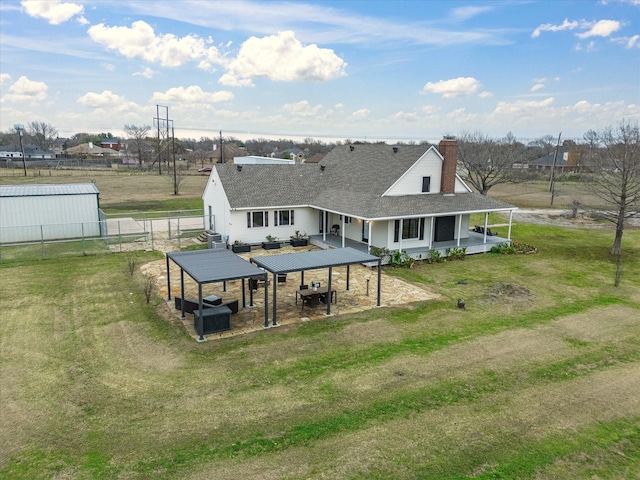 rear view of house featuring a shingled roof, a lawn, a patio, a chimney, and fence