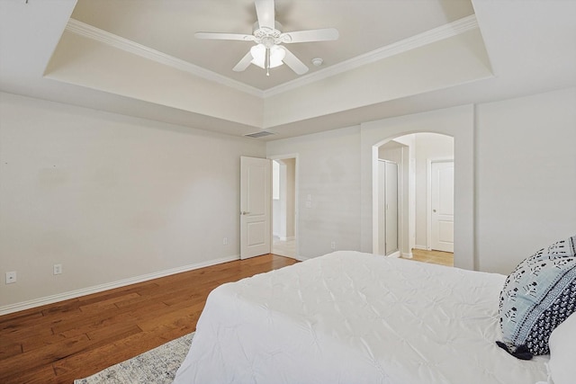 bedroom with wood-type flooring, a raised ceiling, ceiling fan, and crown molding