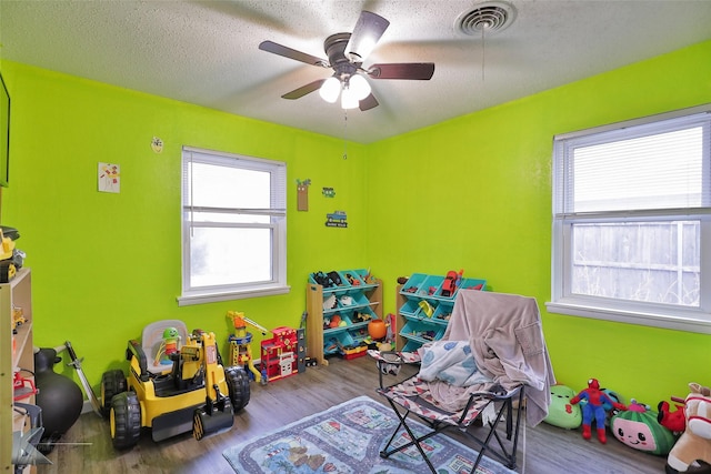 game room featuring a healthy amount of sunlight, ceiling fan, wood-type flooring, and a textured ceiling