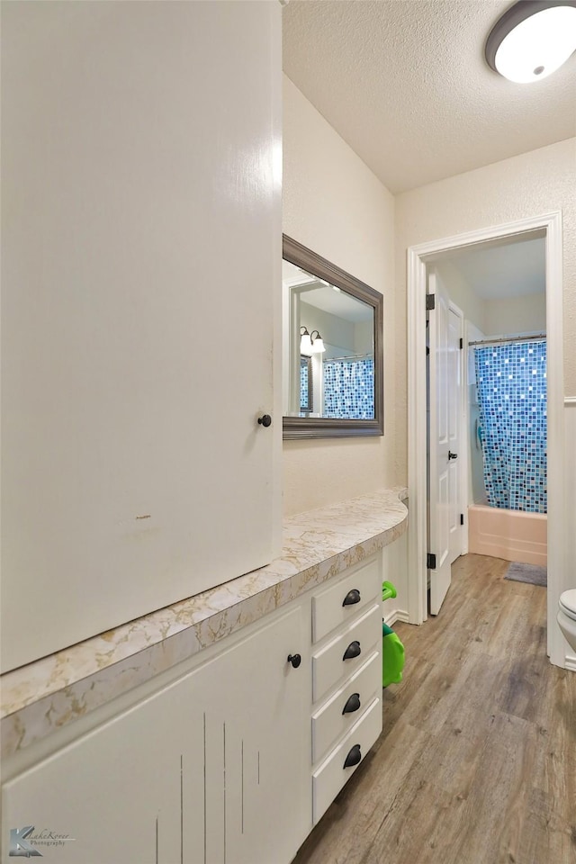 full bathroom with shower / tub combo, vanity, a textured ceiling, hardwood / wood-style flooring, and toilet