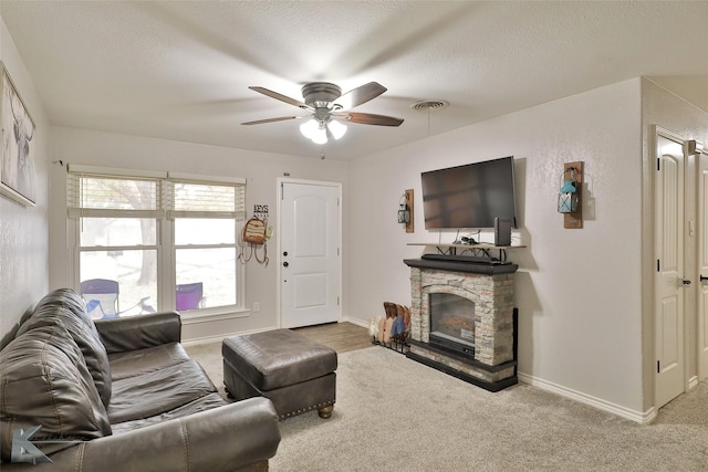 living room with a textured ceiling, light colored carpet, a stone fireplace, and ceiling fan