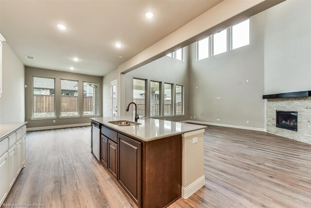 kitchen featuring light wood-type flooring, a stone fireplace, a kitchen island with sink, and sink