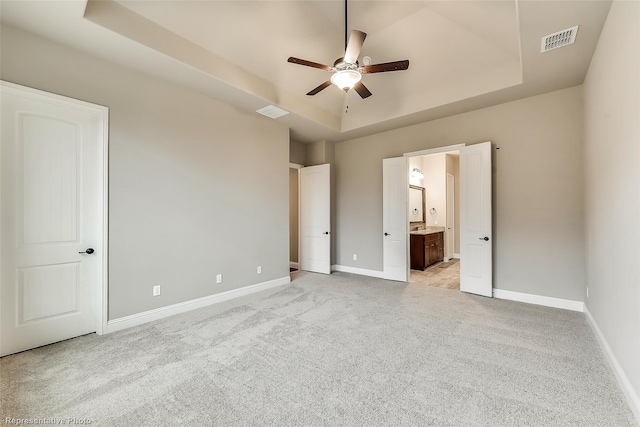 unfurnished bedroom with a tray ceiling, ensuite bathroom, ceiling fan, and light colored carpet