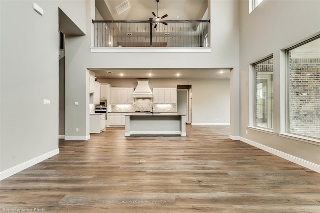 unfurnished living room with a high ceiling, light wood-type flooring, a wealth of natural light, and ceiling fan