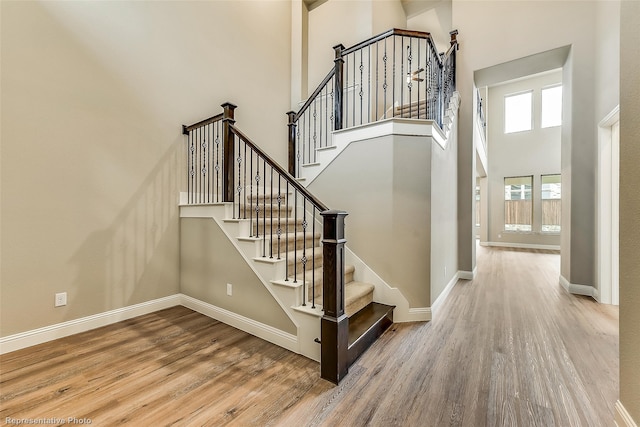 stairway with baseboards, wood finished floors, and a towering ceiling