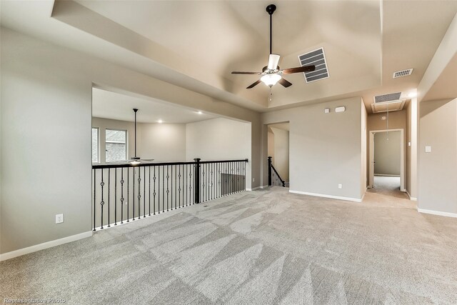 empty room with ceiling fan, light colored carpet, and a tray ceiling