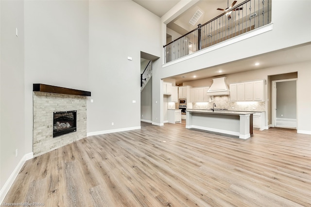 unfurnished living room featuring a high ceiling, light wood-type flooring, ceiling fan, and sink