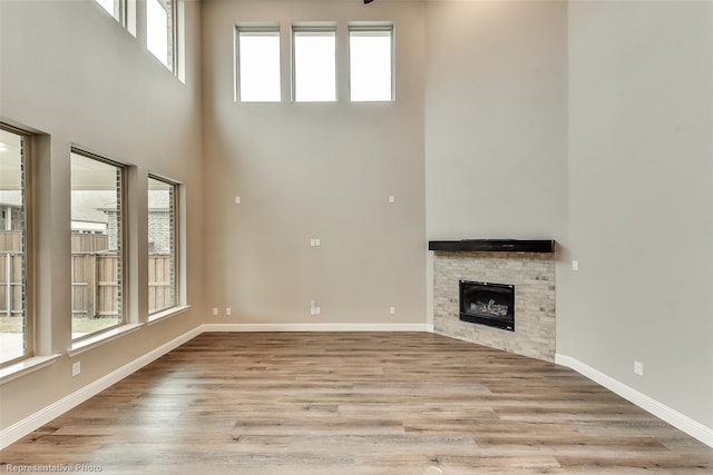 unfurnished living room featuring a towering ceiling, a fireplace, and light hardwood / wood-style flooring