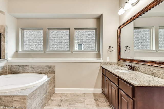 bathroom featuring vanity, a relaxing tiled tub, and a healthy amount of sunlight