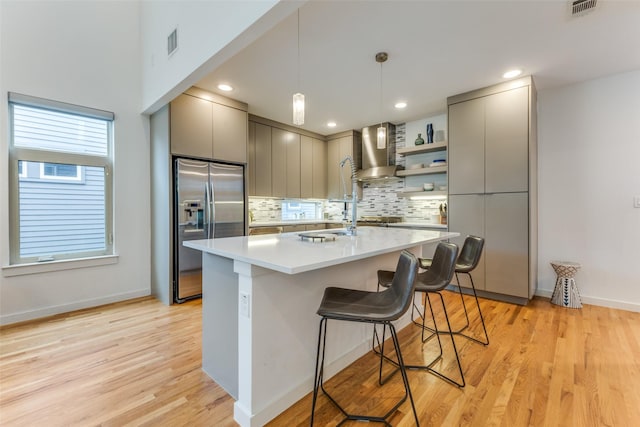 kitchen featuring a breakfast bar, hanging light fixtures, wall chimney exhaust hood, gray cabinets, and stainless steel appliances