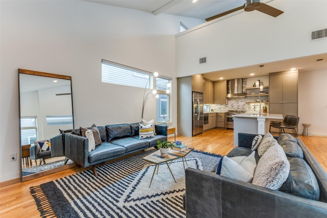 living room with ceiling fan, light wood-type flooring, and a towering ceiling