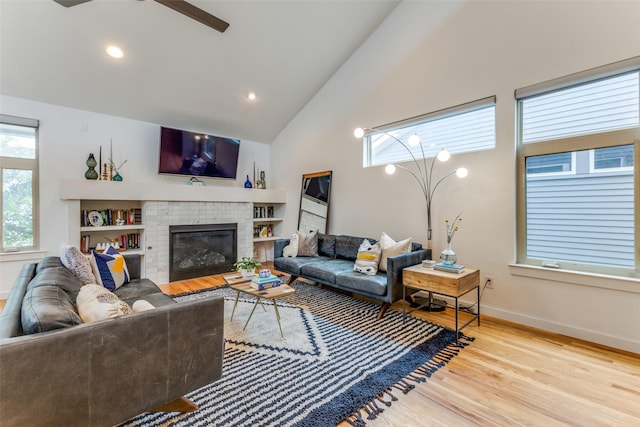 living room featuring ceiling fan, a fireplace, high vaulted ceiling, and light hardwood / wood-style flooring