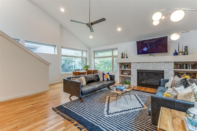 living room featuring built in shelves, ceiling fan, high vaulted ceiling, a fireplace, and light wood-type flooring