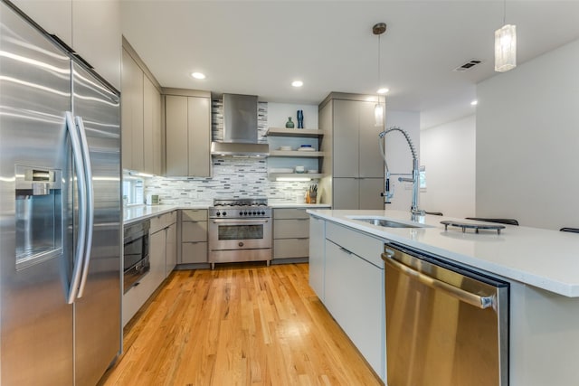 kitchen featuring appliances with stainless steel finishes, gray cabinetry, sink, wall chimney range hood, and decorative light fixtures