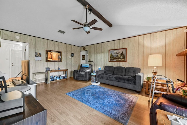 living room with ceiling fan, vaulted ceiling with beams, a textured ceiling, wooden walls, and hardwood / wood-style flooring