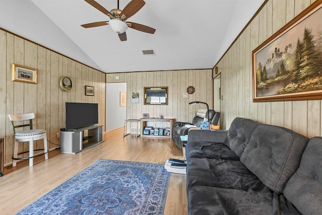 living room featuring ceiling fan, light wood-type flooring, lofted ceiling, and wooden walls