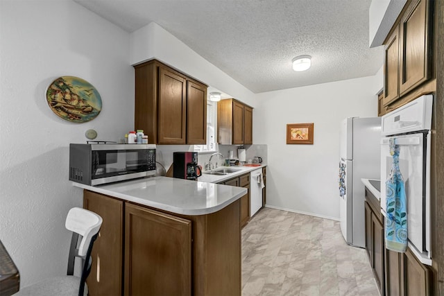 kitchen featuring white oven, sink, a textured ceiling, fridge, and kitchen peninsula