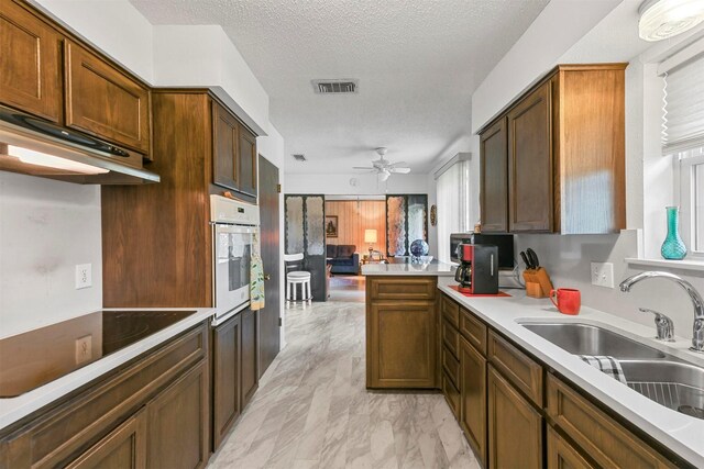 kitchen with white oven, black electric stovetop, sink, a textured ceiling, and kitchen peninsula