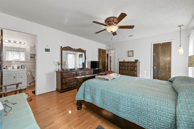 bedroom with hardwood / wood-style floors, ceiling fan, a textured ceiling, and connected bathroom