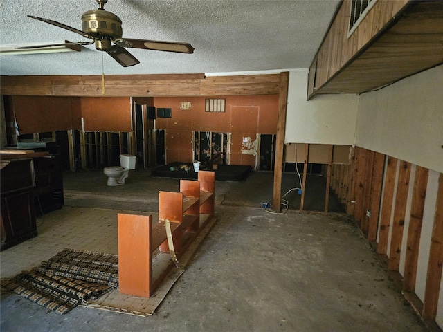 basement with ceiling fan, wood walls, and a textured ceiling