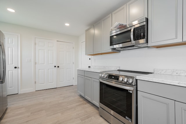 kitchen with gray cabinets, light stone countertops, light hardwood / wood-style floors, and appliances with stainless steel finishes