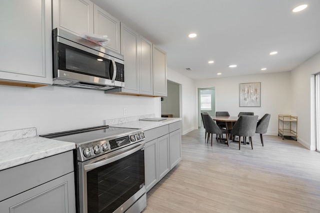 kitchen featuring gray cabinetry, light stone counters, light hardwood / wood-style flooring, and appliances with stainless steel finishes