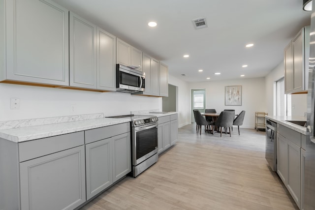 kitchen with gray cabinets, light hardwood / wood-style floors, and appliances with stainless steel finishes